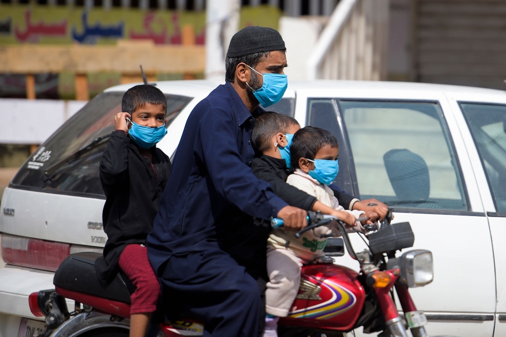 A man and his children wearing facemasks ride on a motorbike along a street during a government-imposed lockdown as a preventive measure against the COVID-19 in Rawalpindi on March 25, 2020. AFP / Farooq Naeem 