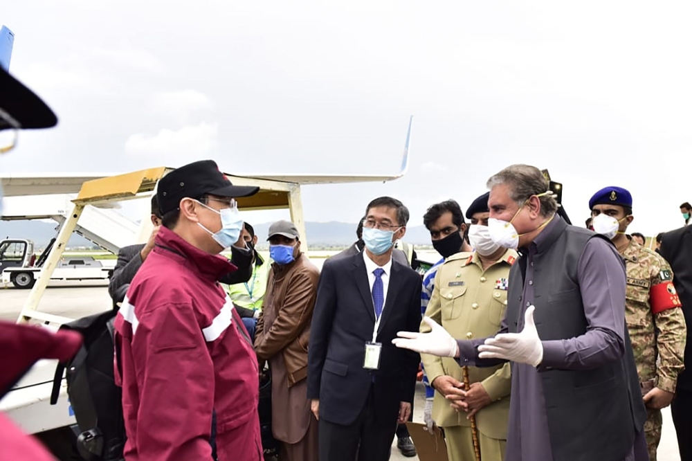In this handout photograph taken and released by the Pakistan's Press Information Department (PID) on March 28, 2020, Pakistan's Foreign Minister Shah Mehmood Qureshi (R) greets Chinese doctors upon their arrival at the Islamabad International airport in 