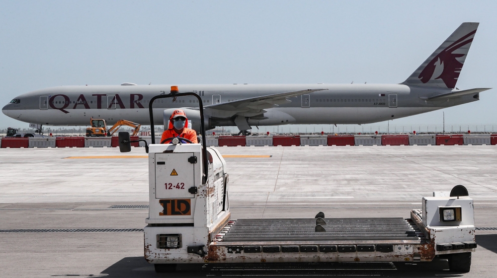 An airport worker mans a luggage trolley while behind him is seen a Qatar Airways Boeing 777 aircraft at Hamad International Airport in the Qatari capital Doha on April 1, 2020. AFP / Karim Jaafar