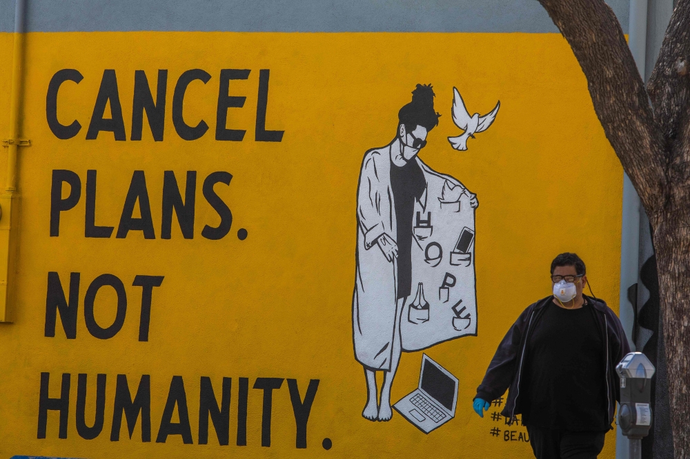 A man wearing gloves and a face mask walks by a mural reading 