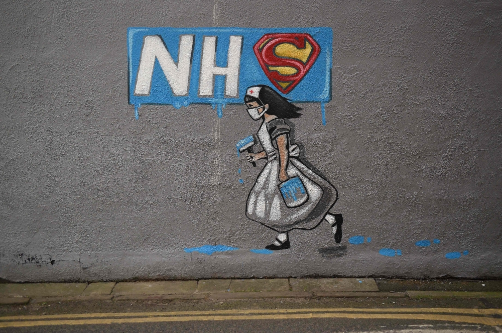 Graffiti depicting the badge of the fictional super heros Superman and Superwoman, and the logo of Britain's National Health Service (NHS) above street art of a nurse, are pictured on a wall in Pontefract, northern England on April 3, 2020, as life in Bri
