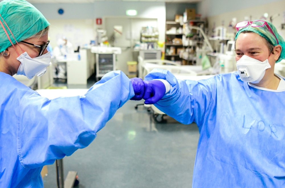 TOPSHOT - Members of the medical staff give themselves a fist bump while working at the intensive care unit (ICU) with the COVID-19 patients at the ASST Papa Giovanni XXIII hospital in Bergamo, on April 3, 2020. / AFP / Piero CRUCIATTI