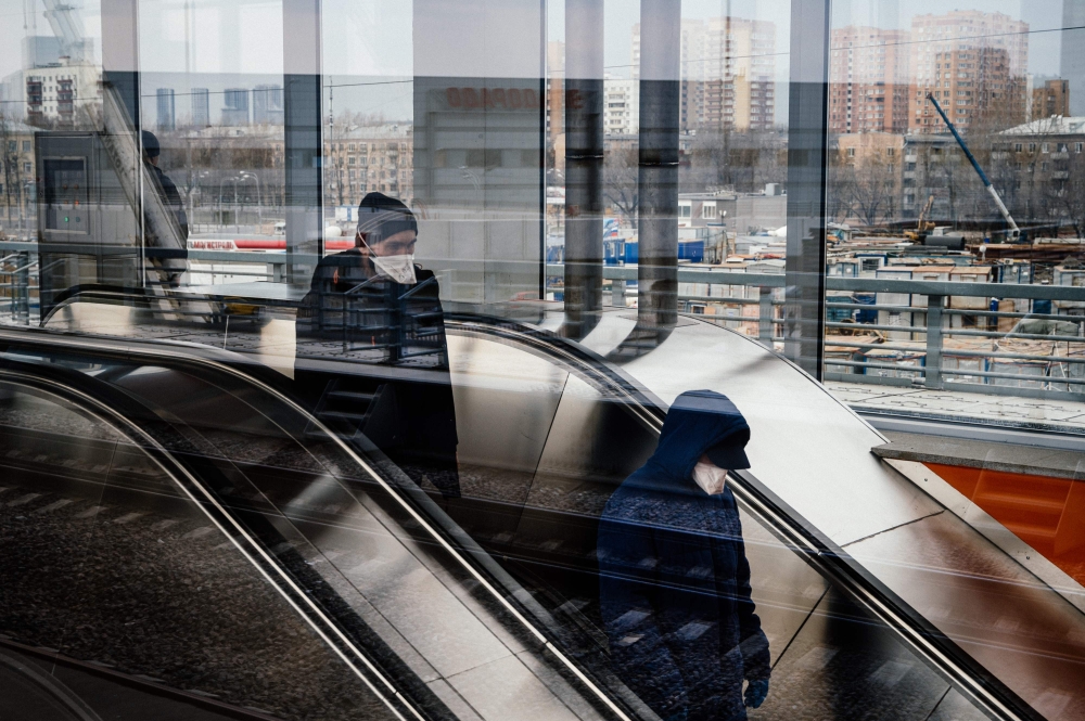 Men wearing face masks ride down an escalator at Nizhegorodskaya station of the Moscow Central Ring, a commuter rail line circling the city, in Moscow on April 8, 2020, during the strict lockdown in Russia to stop the spread of the novel coronavirus COVID