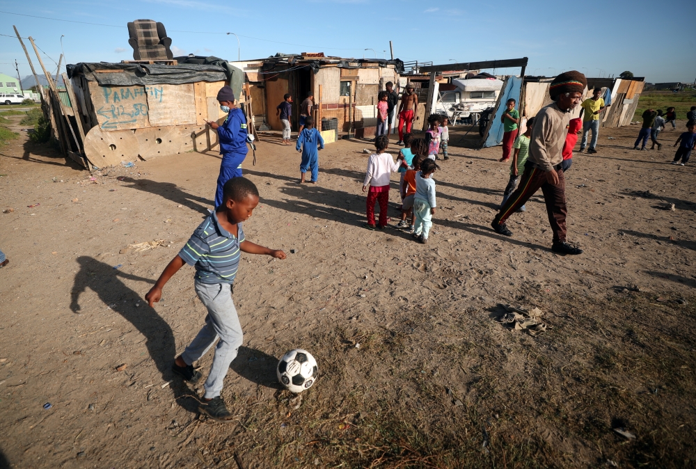 :A township child plays soccer as residents wait to receive food packages handed out by a non governmental organisation during a 21-day nationwide lockdown aimed at limiting the spread of coronavirus disease (COVID-19) in Cape Town, South Africa, April 17