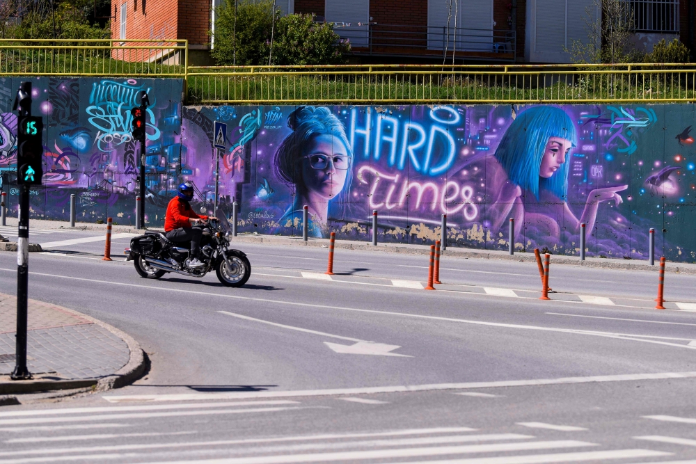 A man rides a motorbike past a graffiti reading 