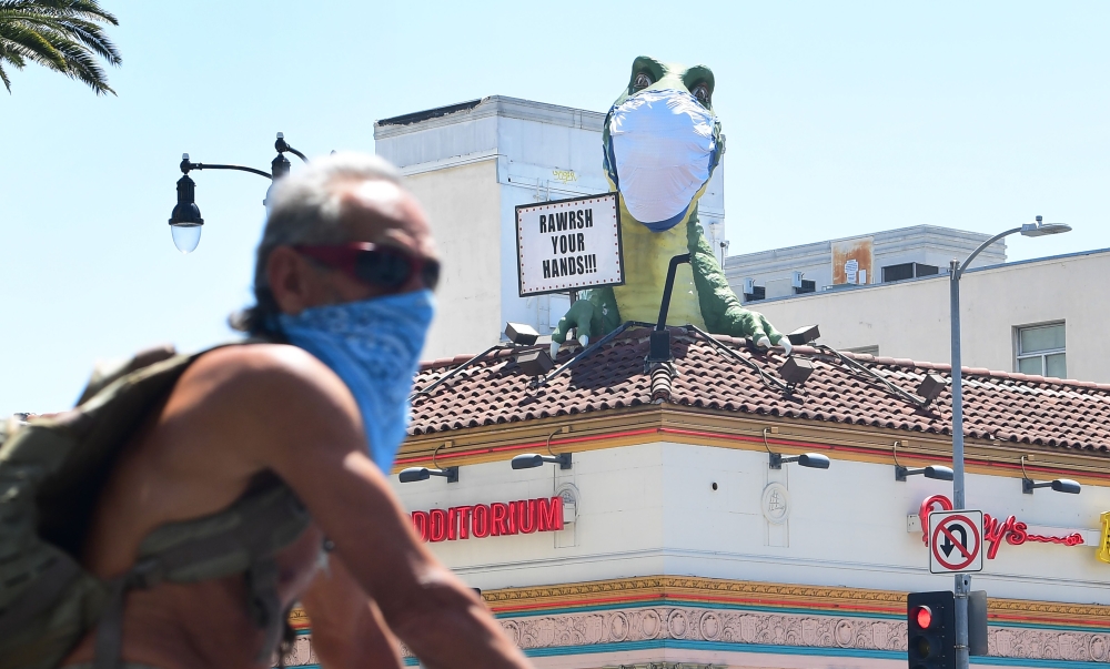 A cyclist wearing facial covering rides past the dinosaur atop the 