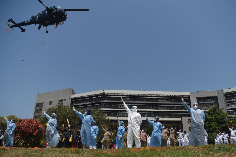 An Indian Navy helicopter (top left) throws rose petals on the INHS Asvini (Indian Naval Hospital Ship) staff to pay tribute to all those involved in the fight against the spread of the COVID-19 coronavirus, in Mumbai on May 3, 2020. / AFP / Punit PARANJP