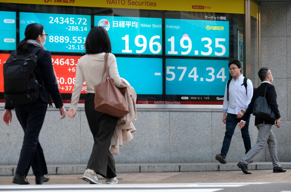 Pedestrians walk in front of a quotation board displaying share prices of the Tokyo Stock Exchange in Tokyo on May 1, 2020. Tokyo stocks closed down more than two percent on May 1 as concerns grew over tensions between the US and China, with traders remai