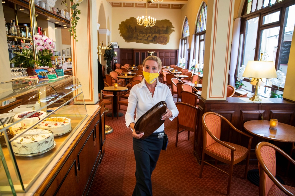 :Antje Roesler works the tables at the reopened Cafe Prag in Schwerin, northeastern Germany on May 9, 2020 amid the ongoing Covid-19, coronavirus pandemic. The traditional cafe and restaurant welcomed sit in customers after two months of closure as restau