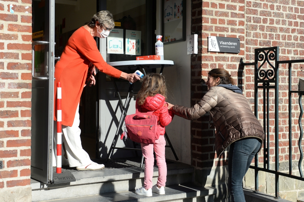 A teacher takes the temperature of a child at the entrance of a flemish primary school during its reopening as a small part of Belgian children head back to their schools with new rules and social distancing during the outbreak of the coronavirus disease 