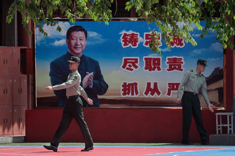 People's Liberation Army (PLA) soldiers are seen next to a poster with a picture of Chinese President Xi Jinping next to the entrance to the Forbidden City in Beijing on May 18, 2020.   AFP / NICOLAS ASFOURI