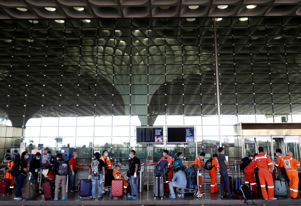 Passengers wearing protective face masks wait in a queue to enter Chhatrapati Shivaji International Airport, after the government allowed domestic flight services to resume, during an extended nationwide lockdown to slow the spread of the coronavirus dise