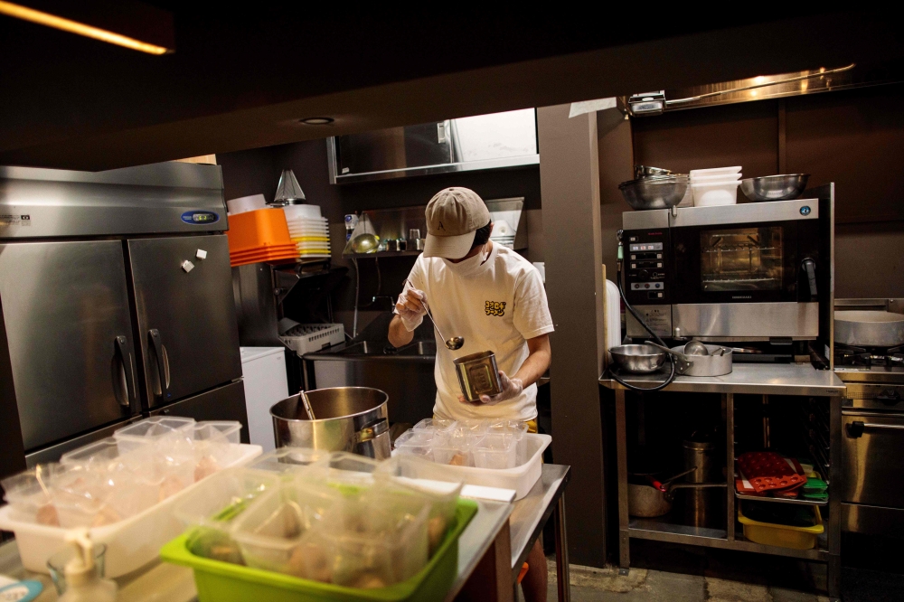 In this picture taken on May 13, 2020 Yuta Shinohara ladles cricket sauce into plastic bags as part of cricket ramen home-cooking kits, at a kitchen in Tokyo. AFP / Behrouz Mehri 