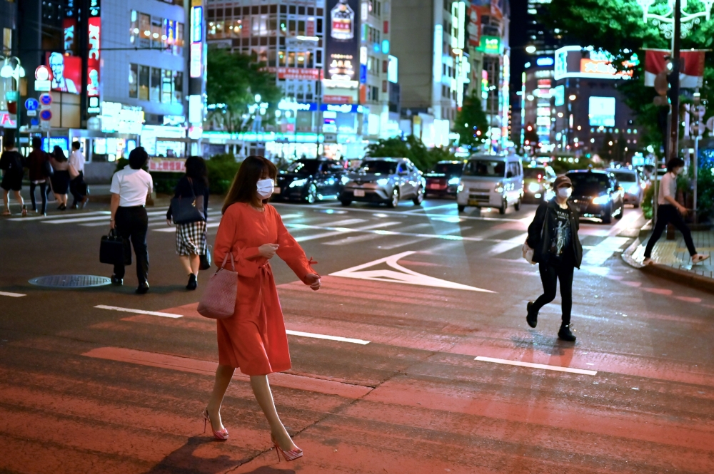 A woman wearing a face mask crosses a street in Tokyo’s Shinjuku area on May 25, 2020. (AFP / CHARLY TRIBALLEAU)