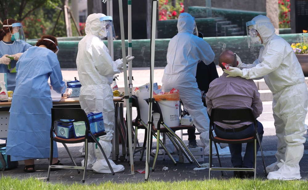 Health workers wearing protective gear take samples from a visitor for the COVID-19 coronavirus test at a temporary virus testing centre in Seoul on May 29, 2020. / AFP / YONHAP /