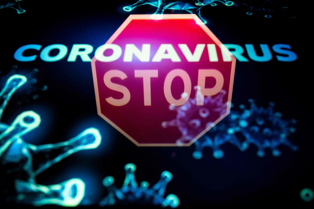 (FILES) This file illustration photo taken on May 10, 2020 in Toulouse shows a stop roadsign reflected on a screen displaying a representation of the novel coronavirus responsible of the COVID-19 disease. / AFP / Lionel BONAVENTURE
