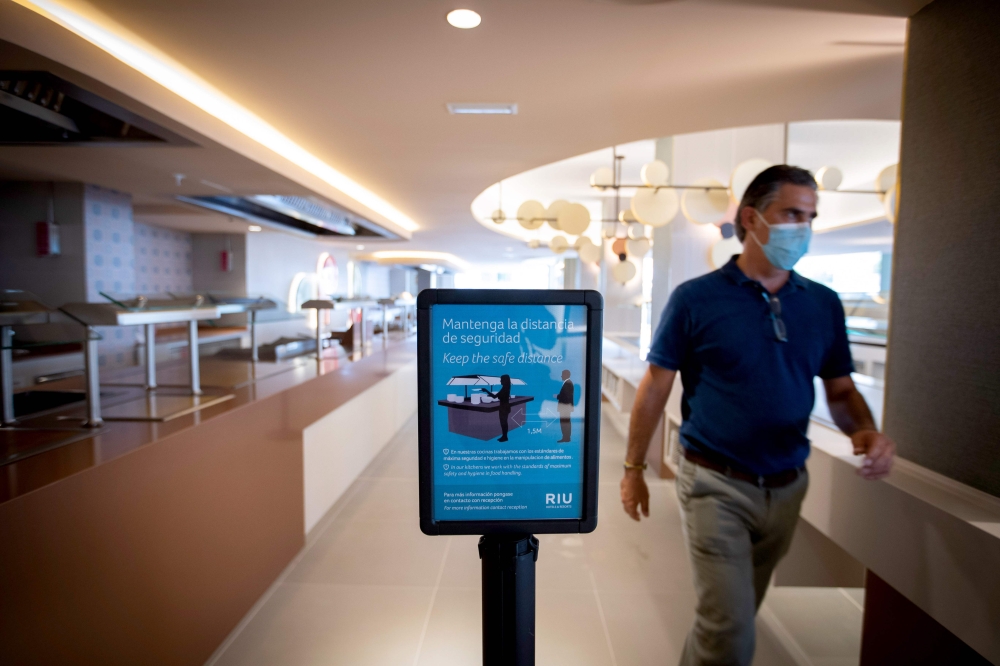 An employee wearing a face mask walks past a sign with security measures at the RIU Concordia Hotel in Palma de Mallorca on June 10, 2020 as the Balearic Islands prepare to welcome German tourists from June 15 as a test before Madrid reopens international