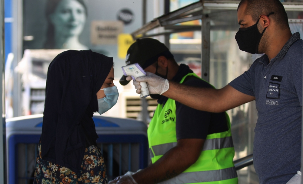 A costumer, wearing a protective mask due to the COVID-19 pandemic, has her temperature checked before entering a supermarket in the Iraqi capital Baghdad, on June 23, 2020. / AFP / AHMAD AL-RUBAYE