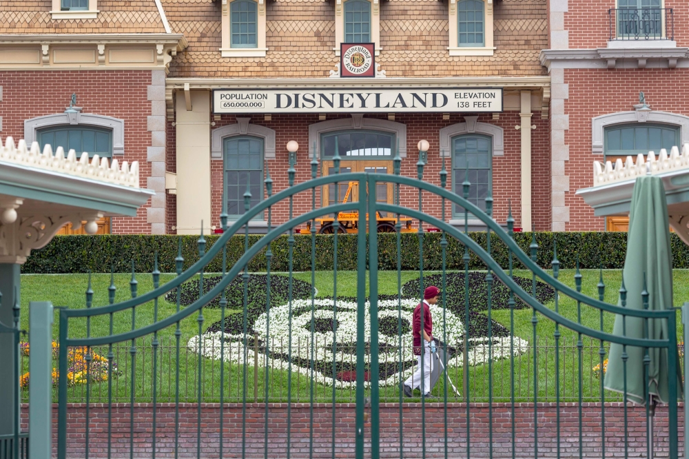 (FILES) In this file photo an employee cleans the grounds behind the closed gates of Disneyland Park on the first day of the closure of Disneyland and Disney California Adventure theme parks as fear of the spread of coronavirus continue, in Anaheim, Calif