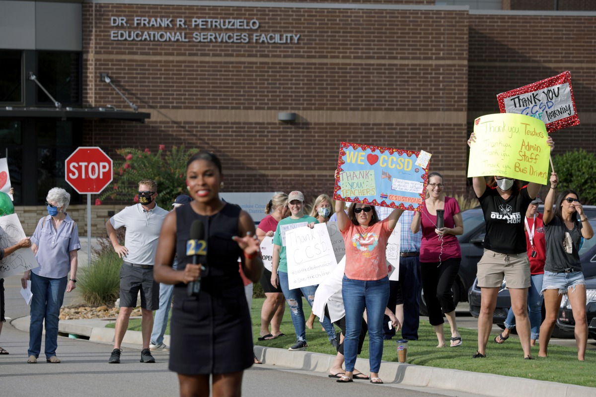 A TV news reporter films a hit in front of supporters of the Cherokee County School District's decision to reopen schools to students during the coronavirus disease (COVID-19) pandemic as they rally outside the district's headquarters, the Dr. Frank R. Pe