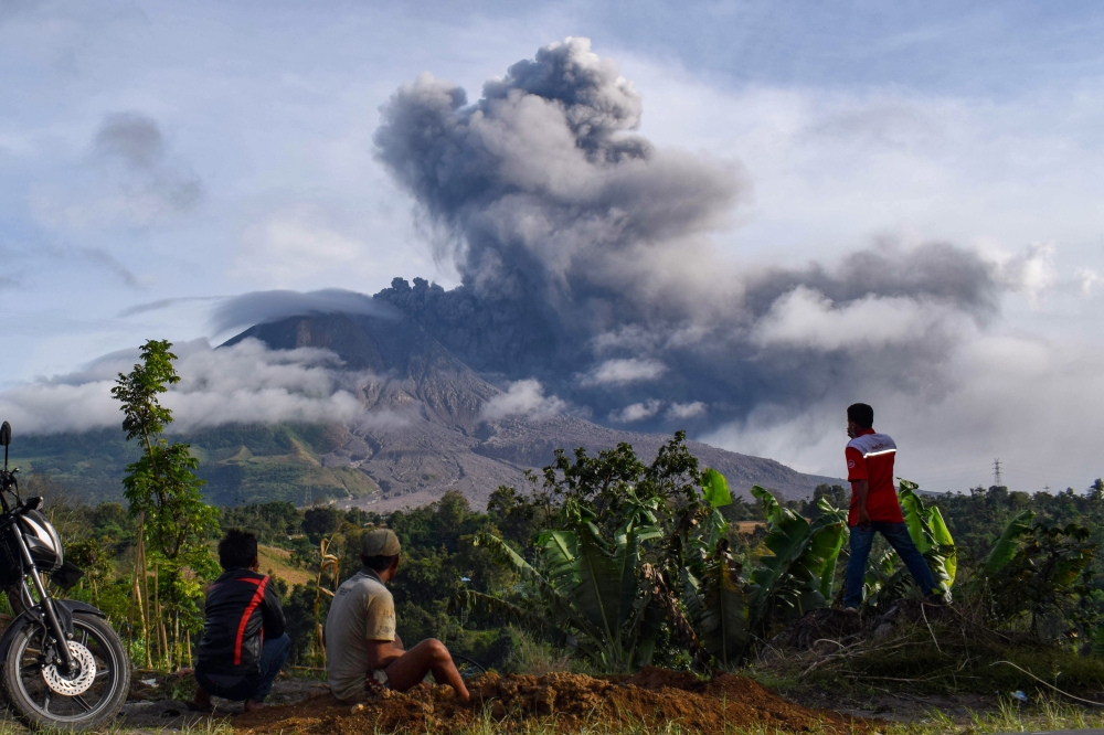 Villagers watch the eruption of Mount Sinabung as seen from Karo, North Sumatra on August 13, 2020. Indonesia's Mount Sinabung erupted again on August 13 with a string of blasts that sent plumes of ash two kilometres (1.2 miles) into sky, triggering a fli