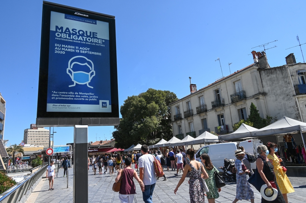 People wearing face masks walk next to a billboard reading: 