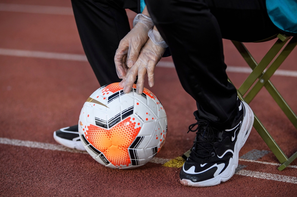 This file photo taken on July 25, 2020 shows a staff member wearing a pair of protective gloves holding a ball during the Chinese Super League (CSL) football match between Guangzhou Evergrande and Shanghai Shenhua in Dalian in China's northeastern Liaonin