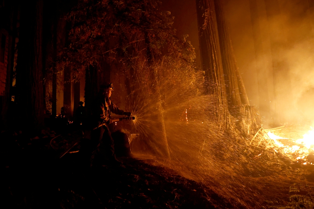 Cal Fire firefighter Anthony Quiroz douses water on a flame as he defends a home during the CZU Lightning Complex Fire in Boulder Creek, California, U.S. August 21, 2020. REUTERS/Stephen Lam