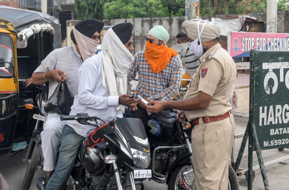 A police personnel (R) checks travel passes from commuters after lockdown norms for weekends and public holidays in the state have been imposed as a preventive measure against the Covid-19 coronavirus, in Amritsar on August 29, 2020. (AFP / NARINDER NANU)
