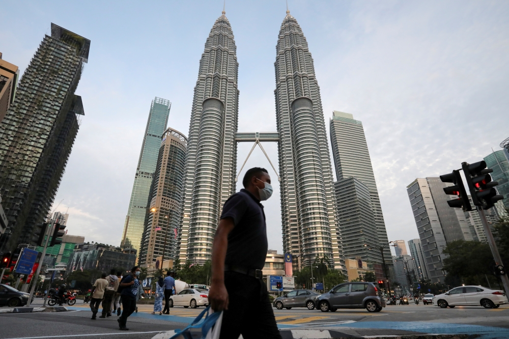 FILE PHOTO: A man wearing a protective mask crosses a street in front of Petronas Twin Towers, amid the coronavirus disease (COVID-19) outbreak in Kuala Lumpur, Malaysia August 11, 2020. REUTERS/Lim Huey Teng