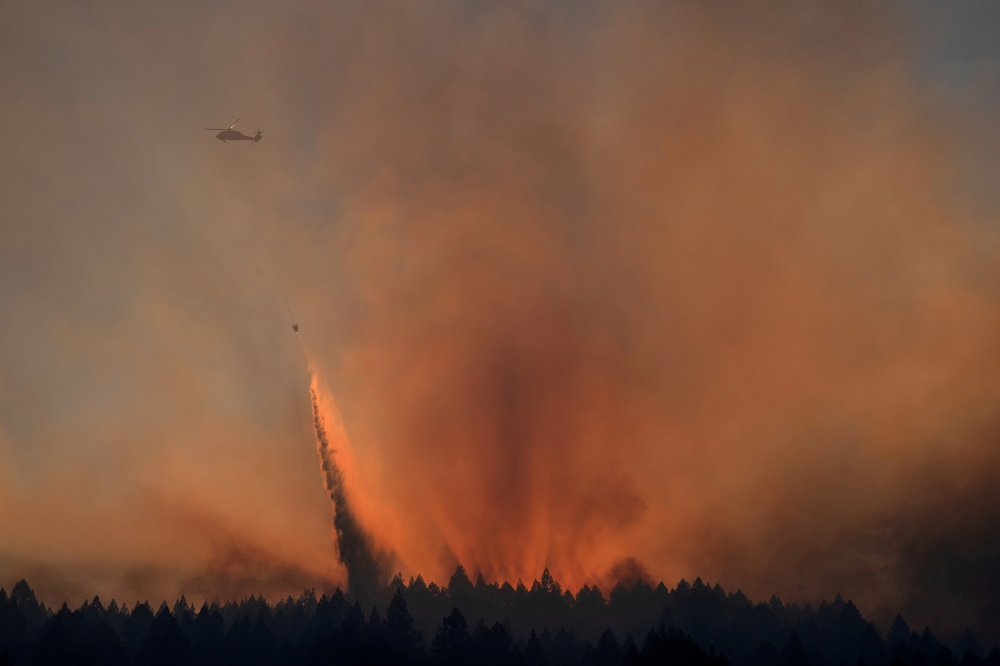 A helicopter is backlit by the sun setting as it drops water over the Bothe-Napa Valley State Park alight from the Glass Fire in Calistoga, California, U.S. October 3, 2020. REUTERS/Adrees Latif