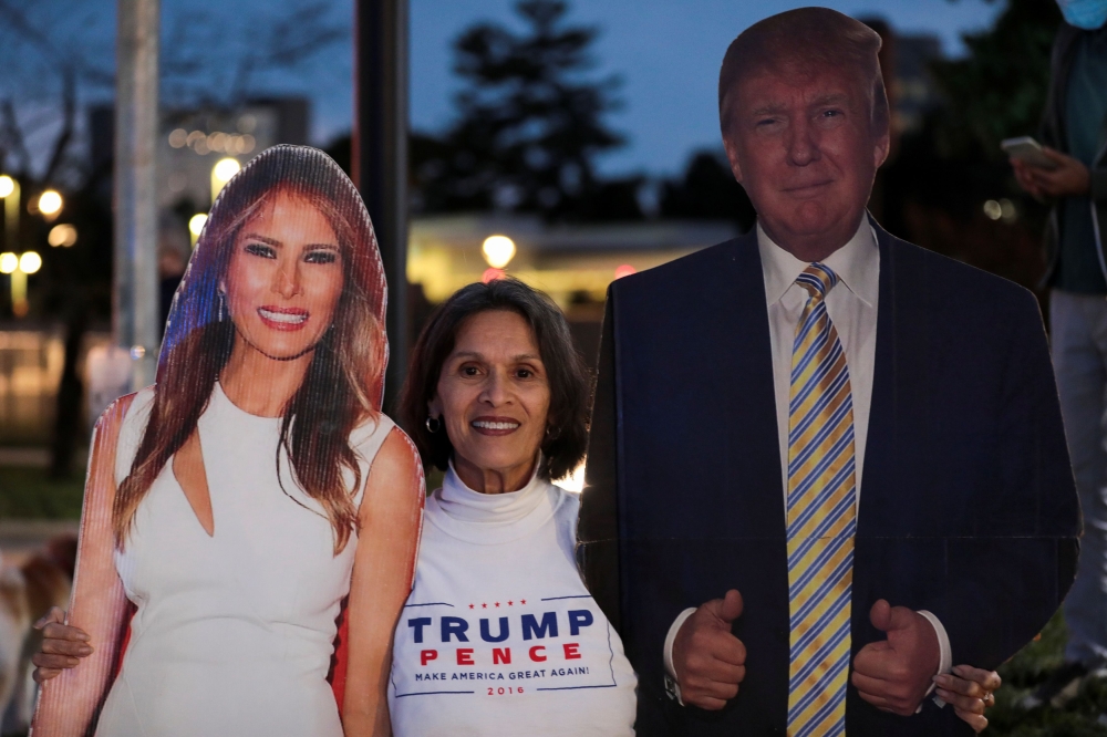A supporter stands in between cardboard cutouts of First Lady Melania Trump and U.S. President Donald Trump, outside of the Walter Reed National Military Medical Center in Bethesda, Maryland, U.S. October 4, 2020. REUTERS/Cheriss May