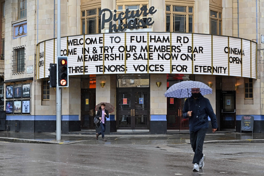 Passers-by shelter under umbrellas outside a Picturehouse cinema in west London on October 4, 2020. Cineworld, which own the Picturehouse chain of cinemas, is set to close its 128 UK sites in the coming weeks. / AFP / JUSTIN TALLIS