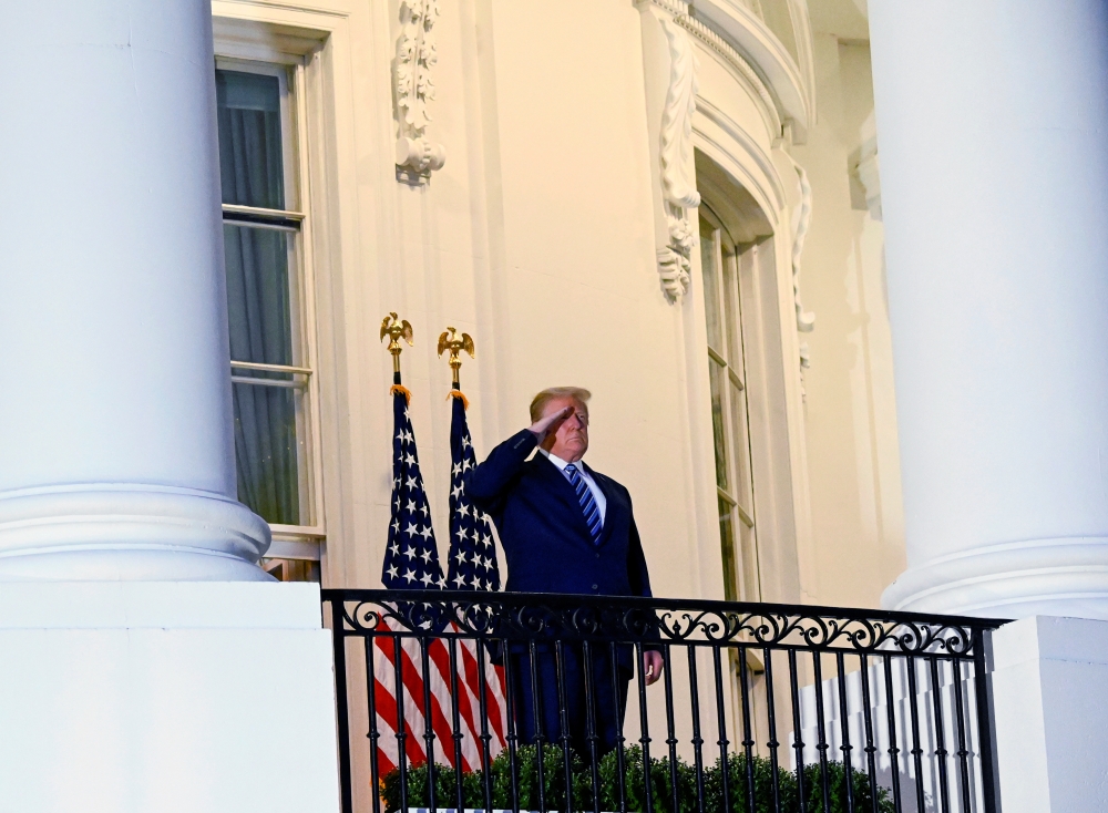 US President Donald Trump salutes as he poses without a face mask on the Truman Balcony of the White House after returning from being hospitalized at Walter Reed Medical Center for coronavirus disease (COVID-19) treatment, in Washington, US October 5, 202