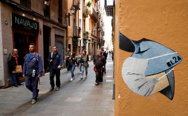FILE PHOTO.People pass near a drawing of a person wearing a mask in a wall, due to the coronavirus outbreak, in central Barcelona, Spain, March 12, 2020. REUTERS/Albert Gea
