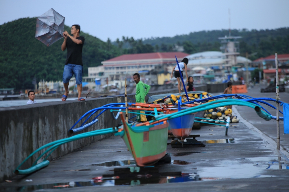 A resident holds onto his umbrella in strong wind as others stand by their wooden boats along the coastal area of Legaspi City, Albay province south of Manila on october 25, 2020, ahead of tropical storm Molave's expected landfall. / AFP / Charism SAYAT