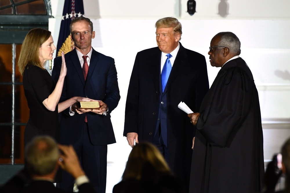US President Donald Trump watches as Supreme Court Associate Justice Clarence Thomas (R) swears in Judge Amy Coney Barrett as a US Supreme Court Associate Justice, flanked by her husband Jesse M. Barrett, during a ceremony on the South Lawn of the White H