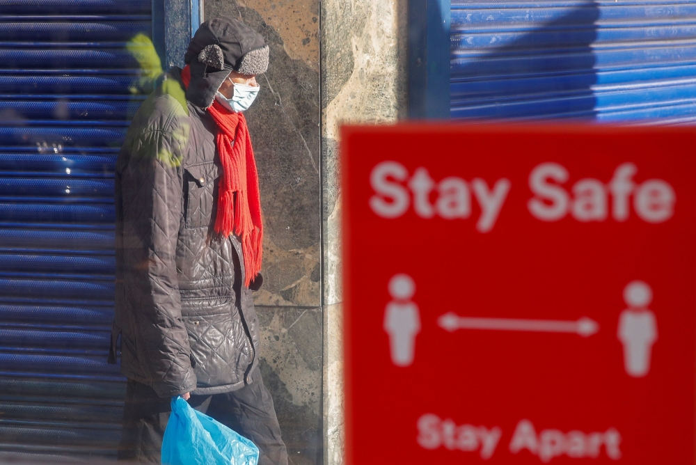 FILE PHOTO: A person wearing a protective mask walks near a social distancing sign, amid the outbreak of the coronavirus disease (COVID-19), in Coventry, Britain October 25, 2020. Reuters/Andrew Couldridge/File Photo
