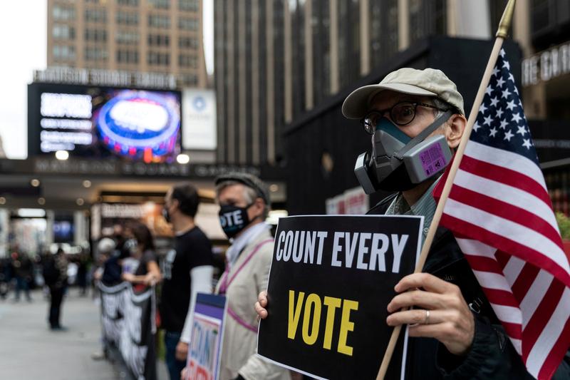 FILE PHOTO: A man wearing a protective mask due to COVID-19 pandemic holds a sign outside Madison Square Garden, which is used as a polling station, on the first day of early voting in Manhattan, New York, U.S. October 24, 2020. REUTERS/Jeenah Moon/File P
