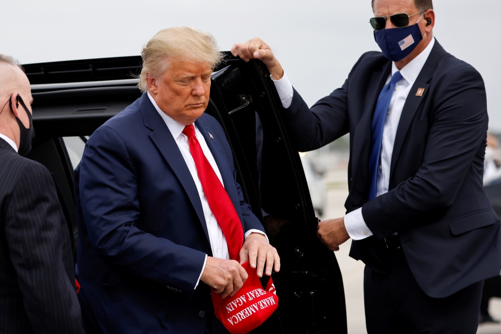 FILE PHOTO: U.S. President Donald Trump holds a 'Make America Great Again' cap while arriving to board Air Force One as he departs Florida for campaign travel to North Carolina, Pennsylvania, Michigan and Wisconsin at Miami International Airport in Miami,