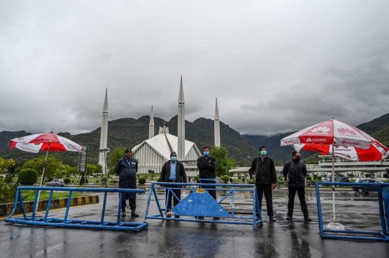 FILE PHOTO: Policemen wearing facemasks stand guard at a checkpoint beside the Grand Faisal Mosque during a government-imposed nationwide lockdown as a preventive measure against the COVID-19 coronavirus, in Islamabad on March 27, 2020. / AFP / Aamir QURE