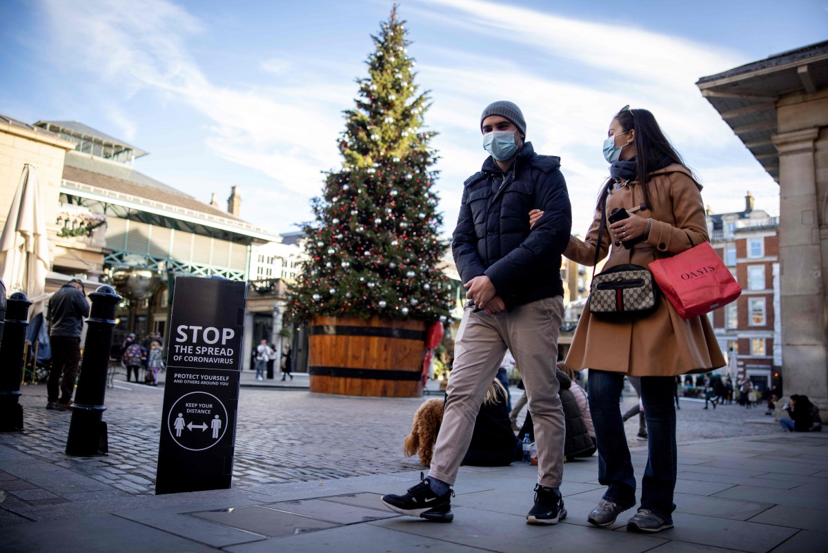 Pedestrians wearing a protective face covering to combat the spread of the coronavirus, pass COVID-19 information sign reading 
