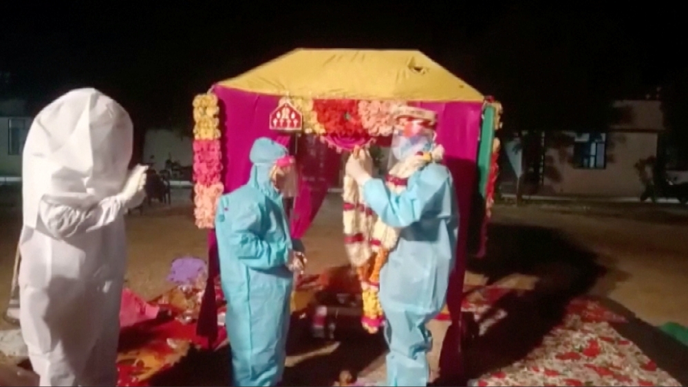 A bride and groom wearing personal protective equipment (PPE) exchange flower garlands during a wedding ritual in Baran, Rajasthan, India December 6, 2020, in this still image taken from video. ANI/Reuters 