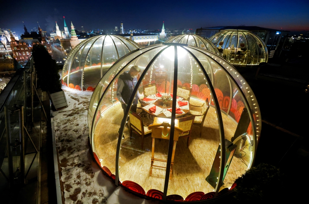 A waiter sets a table inside a transparent pod offered for private Christmas meals with backdrop of the Kremlin and Red Square on the rooftop of Ritz-Carlton hotel in Moscow, Russia December 8, 2020. Picture taken December 8, 2020. REUTERS/Maxim Shemetov 