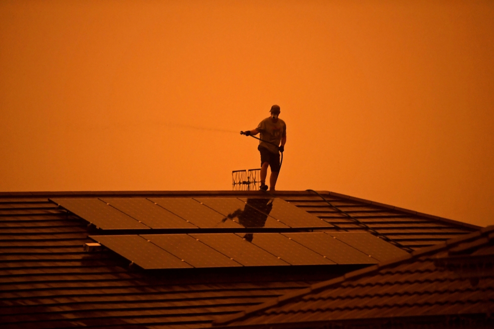 A resident uses a garden hose to wet down the house as high winds push smoke and ash from the Currowan Fire towards Nowra, New South Wales, Australia January 4, 2020. REUTERS/Tracey Nearmy/File Photo/File Photo