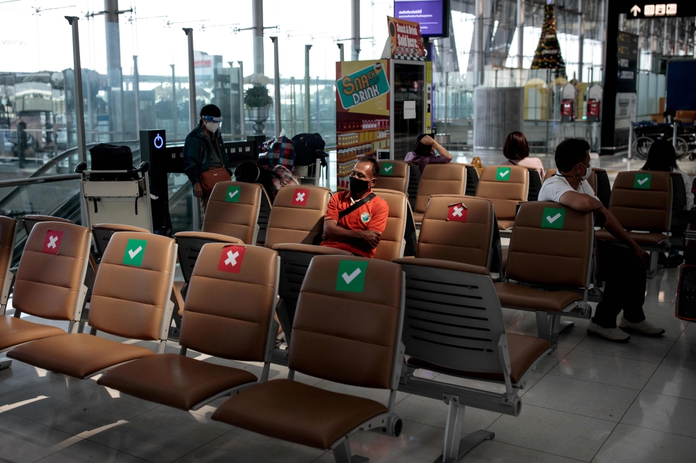 A man wearing a face mask as a preventative measure against Covid-19 coronavirus sits in the departure terminal of Suvarnabhumi International Airport in Bangkok on December 18, 2020. / AFP / Jack TAYLOR