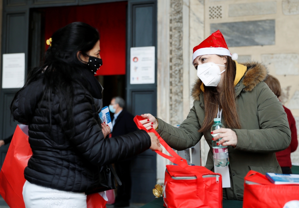 A woman receives a meal from a member of Rome-based charity Sant'Egidio Community in the church of Santa Maria in Trastevere, in Rome, Italy, December 25, 2020. (REUTERS/Yara Nardi)