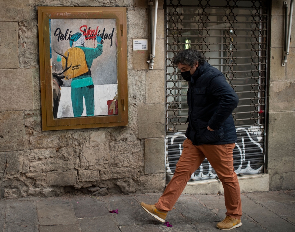 A man walks past a new work by Italian street artist TvBoy depicting Santa Claus carrying the Covid-19 vaccine in his sack, in Barcelona on December 24, 2020.   / AFP / Josep LAGO