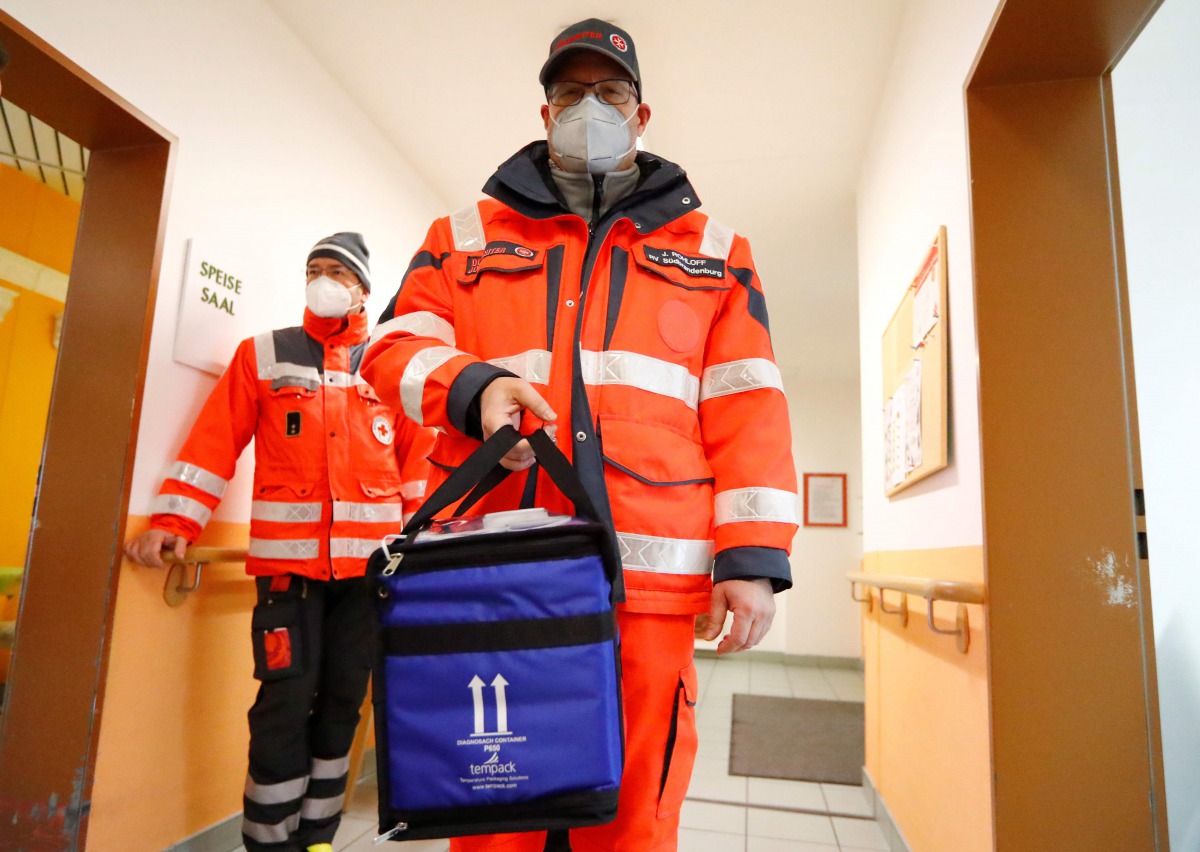 A medical worker carries a box of vials containing the Pfizer-BioNTech COVID-19, coronavirus vaccine during an inoculation program at a care home in Grossraeschen, eastern Germany , on December 27, 2020. / AFP / POOL / FABRIZIO BENSCH