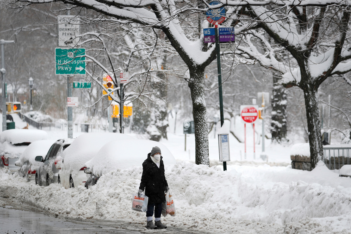 A woman holds shopping bags as she waits at a bus stop near deep snow banks on Manhattan's Upper West Side after a winter storm in New York City, New York, U.S., February 2, 2021. REUTERS/Mike Segar
